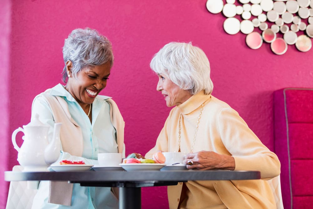 Two Charter Senior Living of Hopkinsville residents smile and share tea and snacks together at a table Two Charter Senior Living of Hopkinsville residents smile and share tea and snacks together at a table