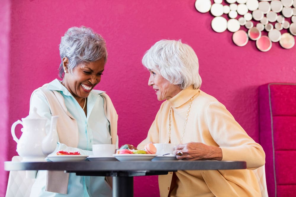 Two Charter Senior Living of Hopkinsville residents smile and share tea and snacks together at a table 